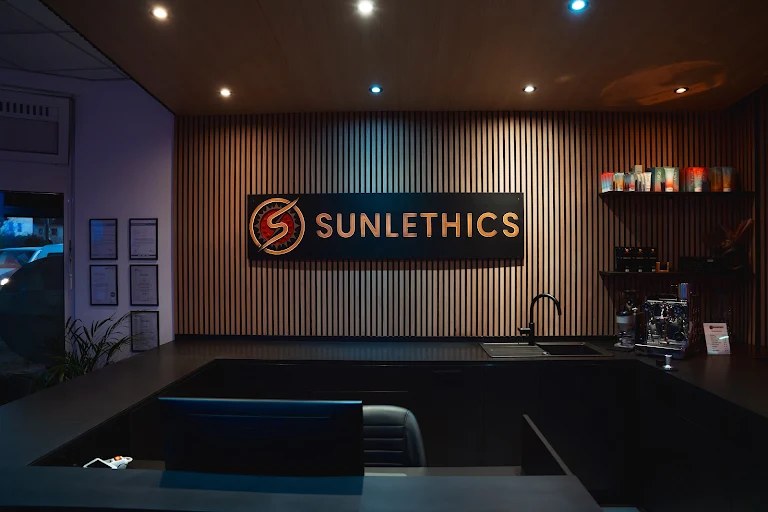 Empfangstheke bei SUNLETHICS mit beleuchtetem Logo an der Holzlamellenwand